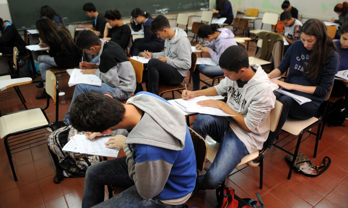 Estudante se preparando para o Enem com material e dispositivo eletrônico