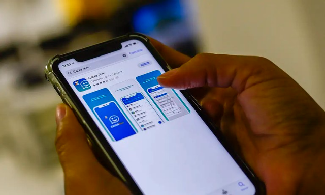 Mãos seguram celular com a página do aplicativo Caixa Tem aberta na loja de aplicativos