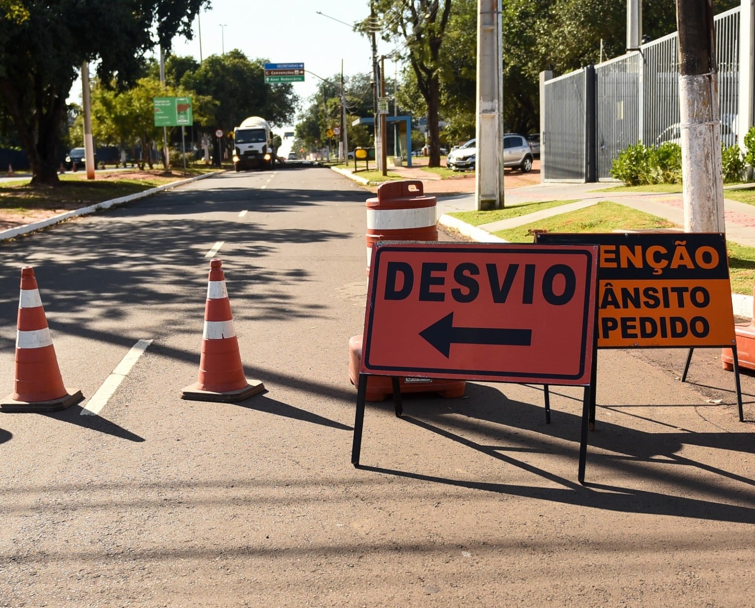 Cones laranja e placa vermelha com a palavra «Desvio» e seta bloqueando uma rua asfaltada