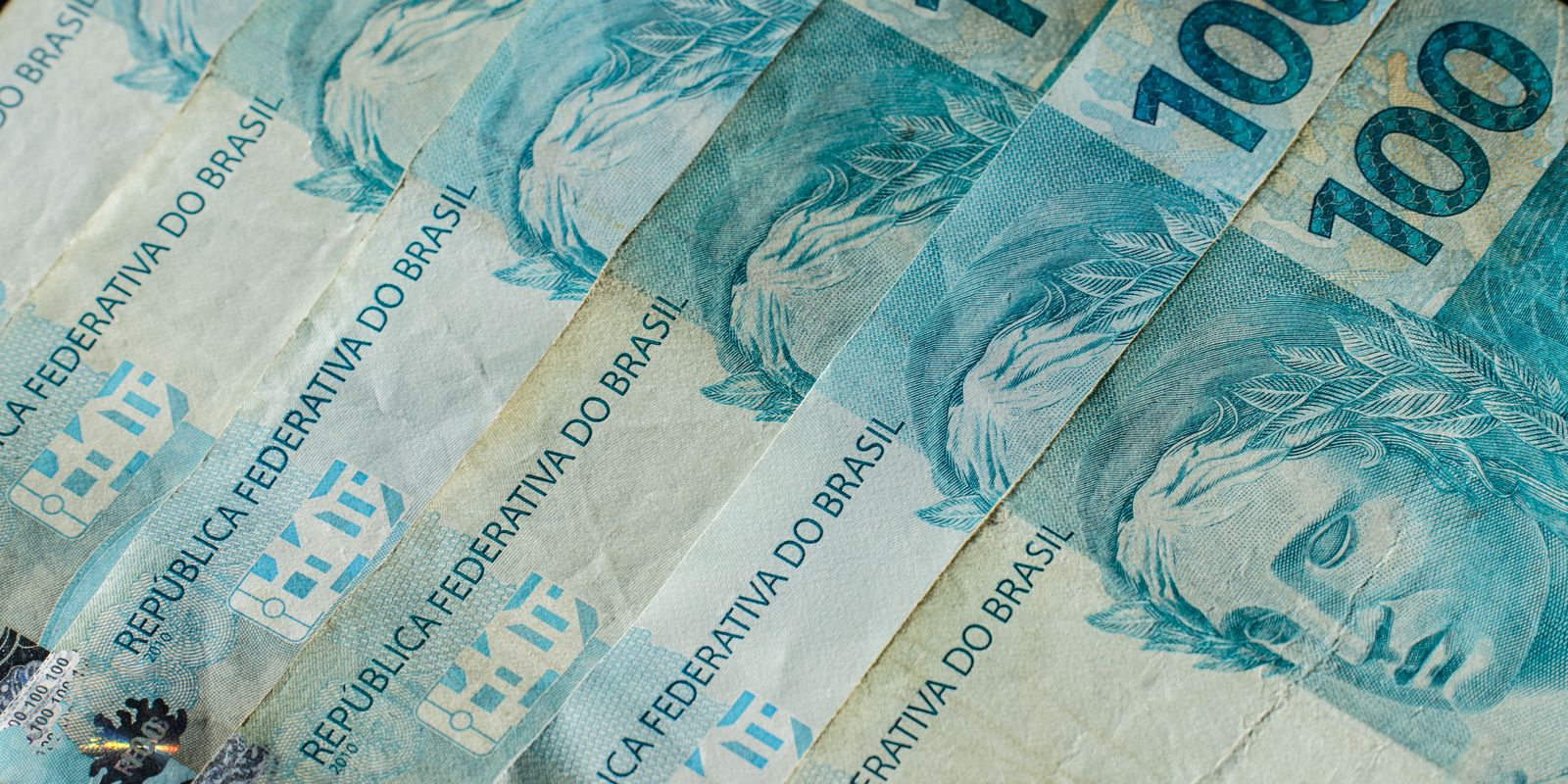 Várias cédulas de 100 reais enfileiradas, em close