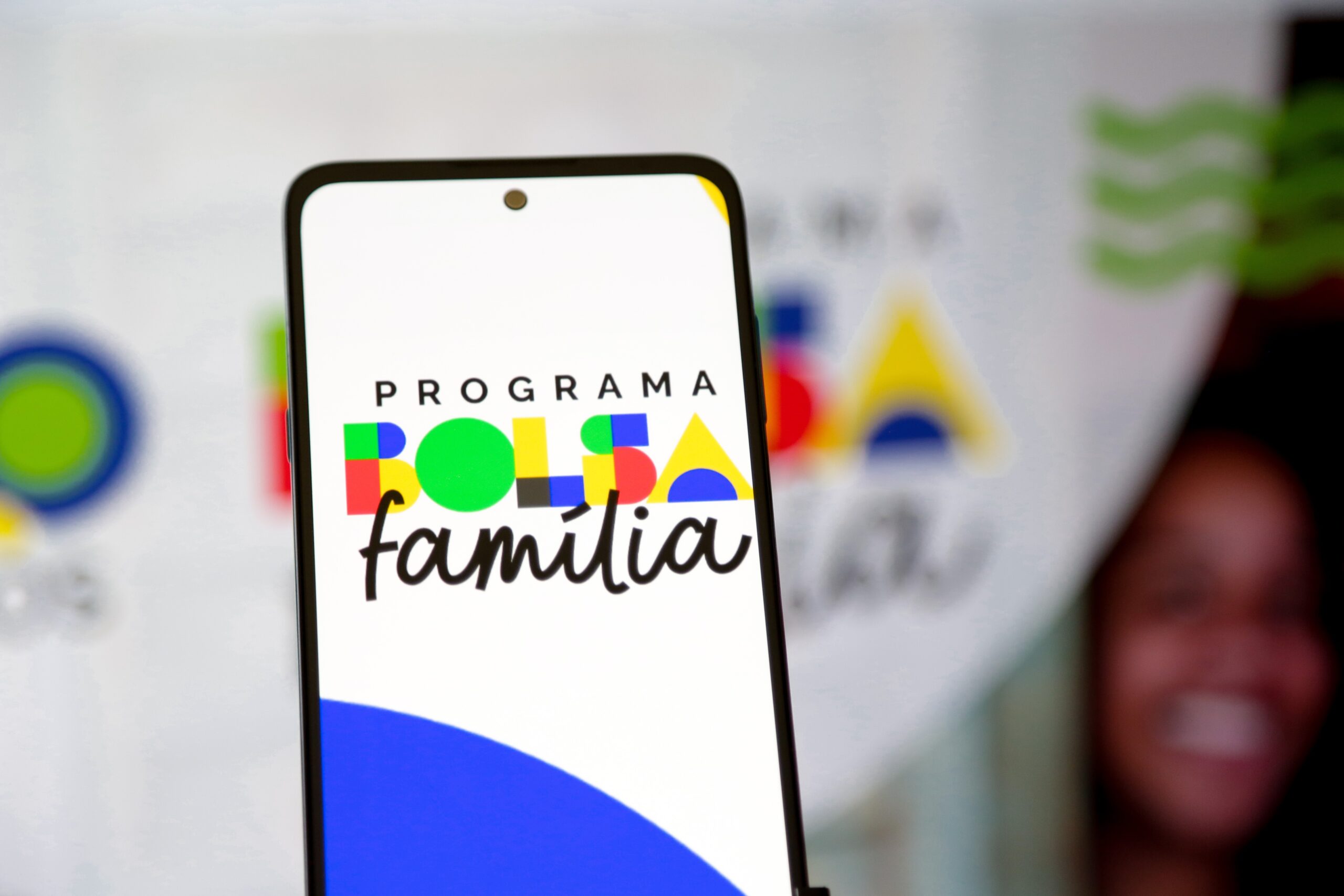 Celular com a tela do aplicativo do Programa Bolsa Família em primeiro plano, com fundo desfocado