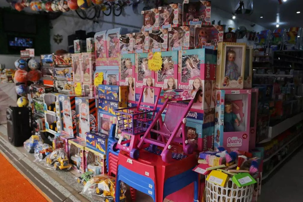 Brinquedos em caixas, bonecas e carrinhos infantis expostos na entrada de uma loja