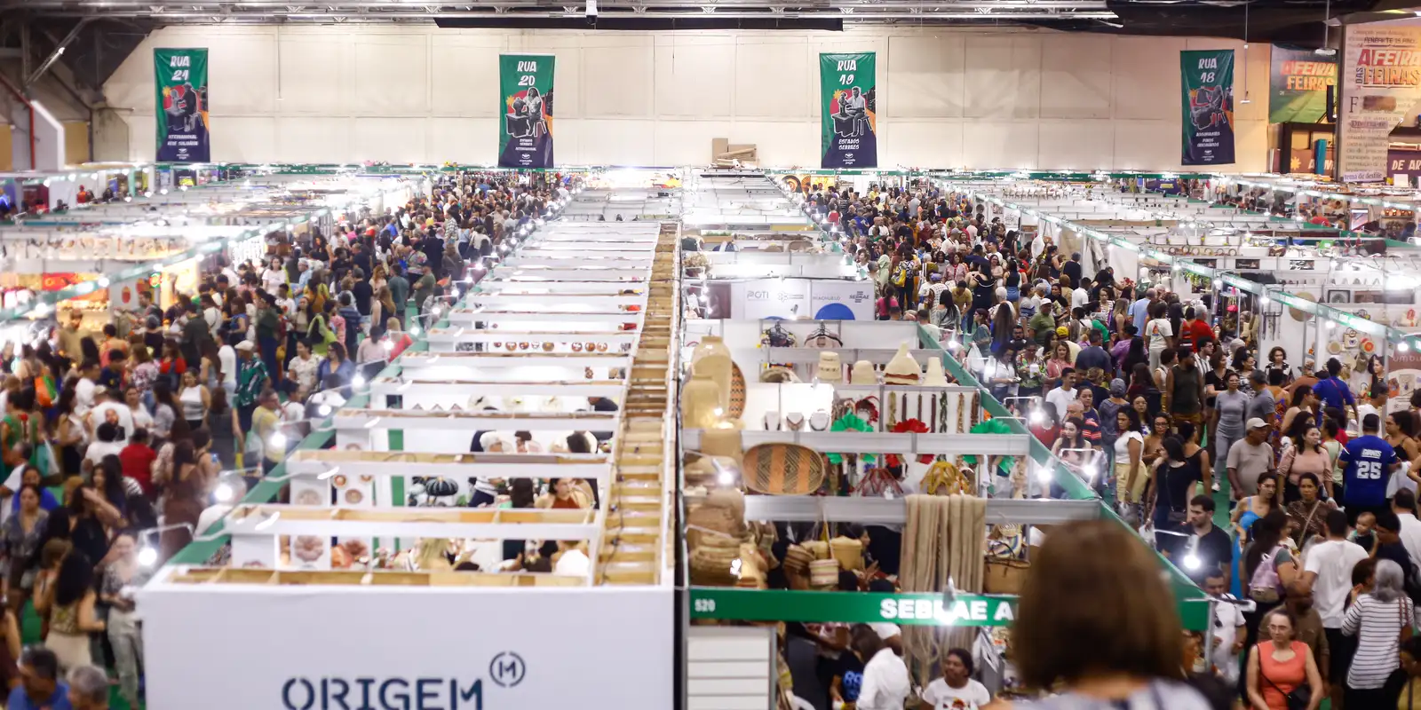 Pavilhão de feira lotado, com corredores de estandes de pequenos empreendedores