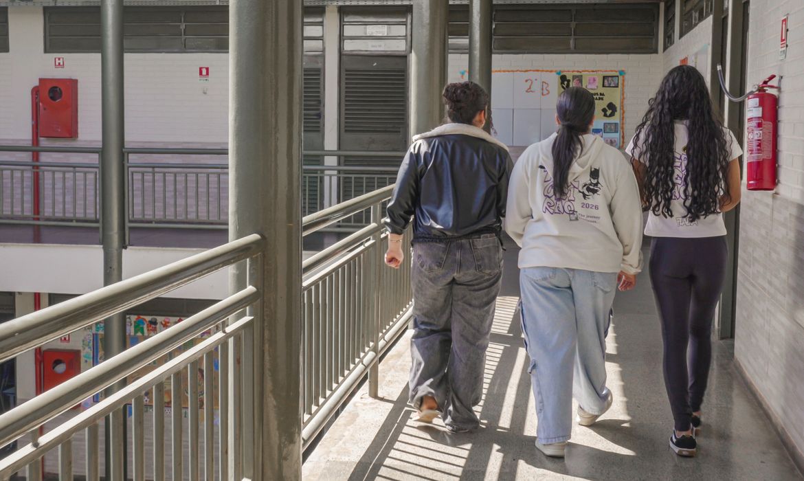 Estudantes fazem anotações em cadernos sentados em carteiras numa sala de aula