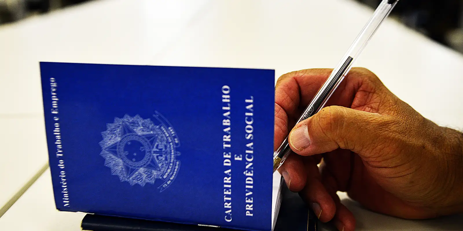 Mão segura caneta sobre carteira de trabalho azul aberta em uma mesa