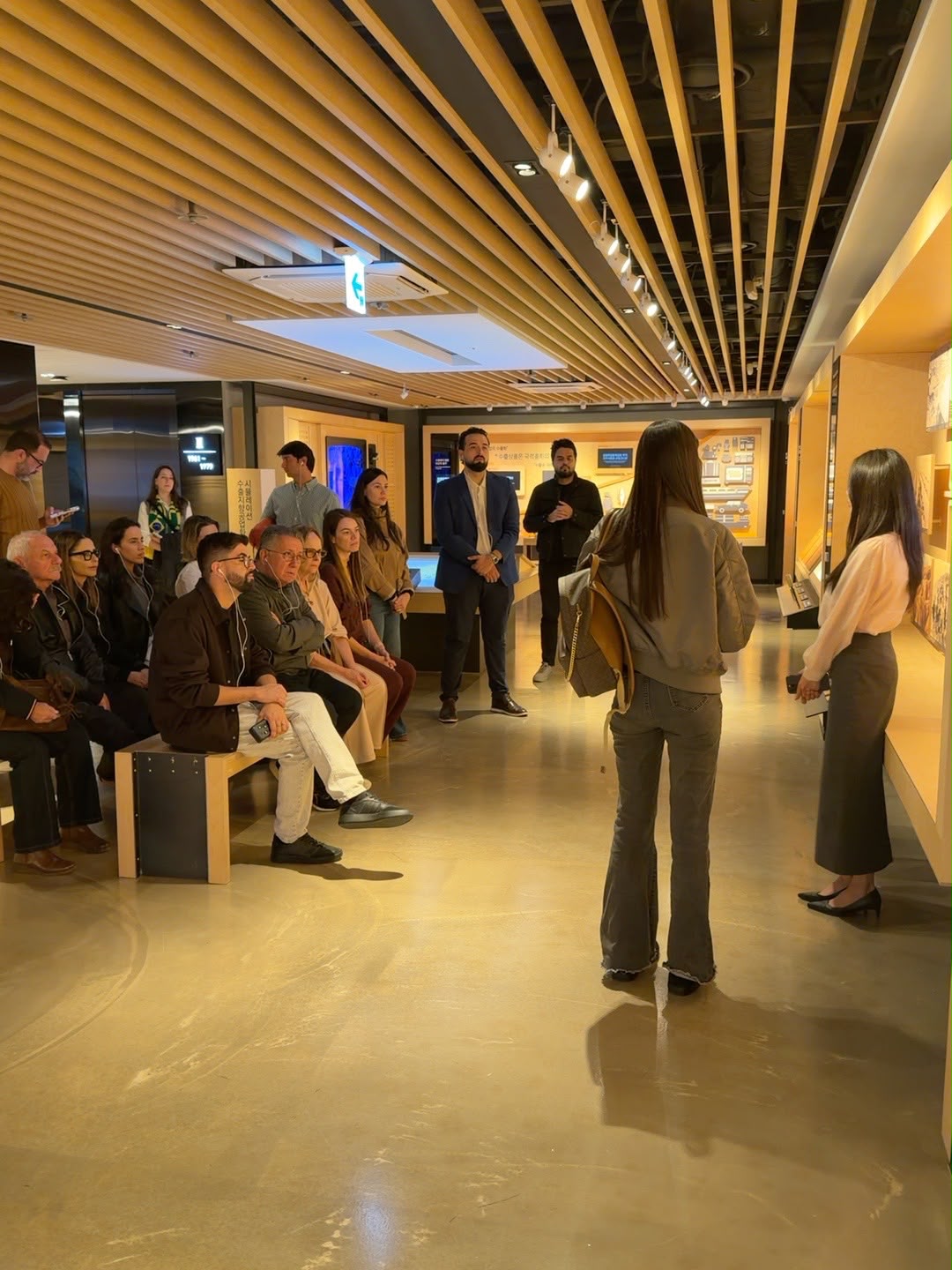 Empresários sentados em bancos ouvem guia durante visita a exposição em Seul