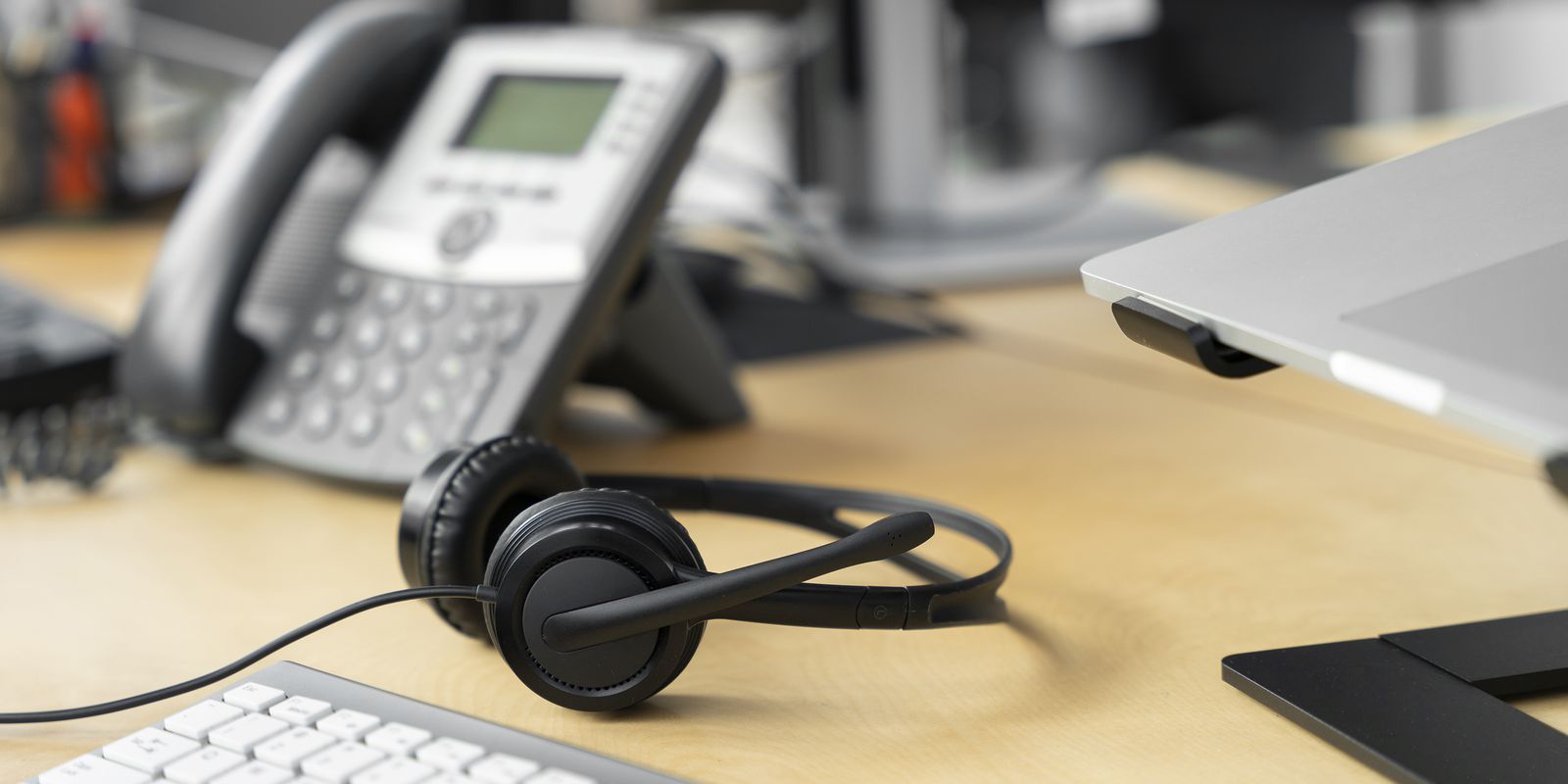 Fone de ouvido com microfone de call center sobre mesa, ao lado de telefone e teclado