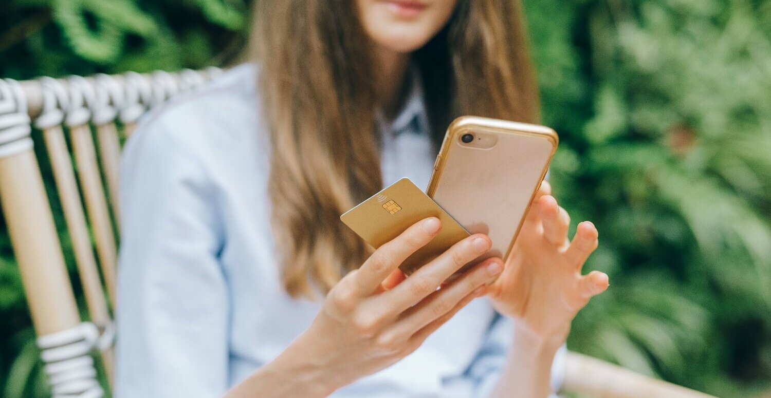 Pessoa segura cartão bancário e celular para conferir pagamento