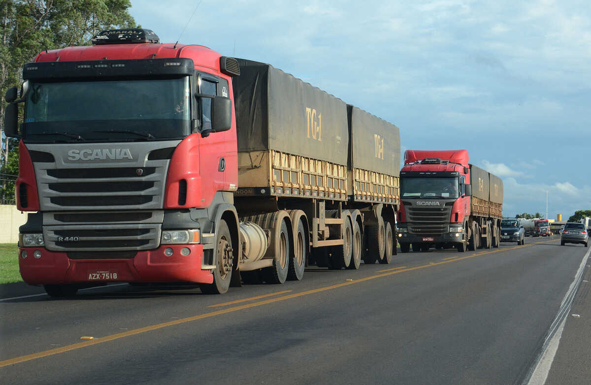 Duas carretas bitrem com cabines vermelhas trafegando por rodovia de pista simples, com carros atrás