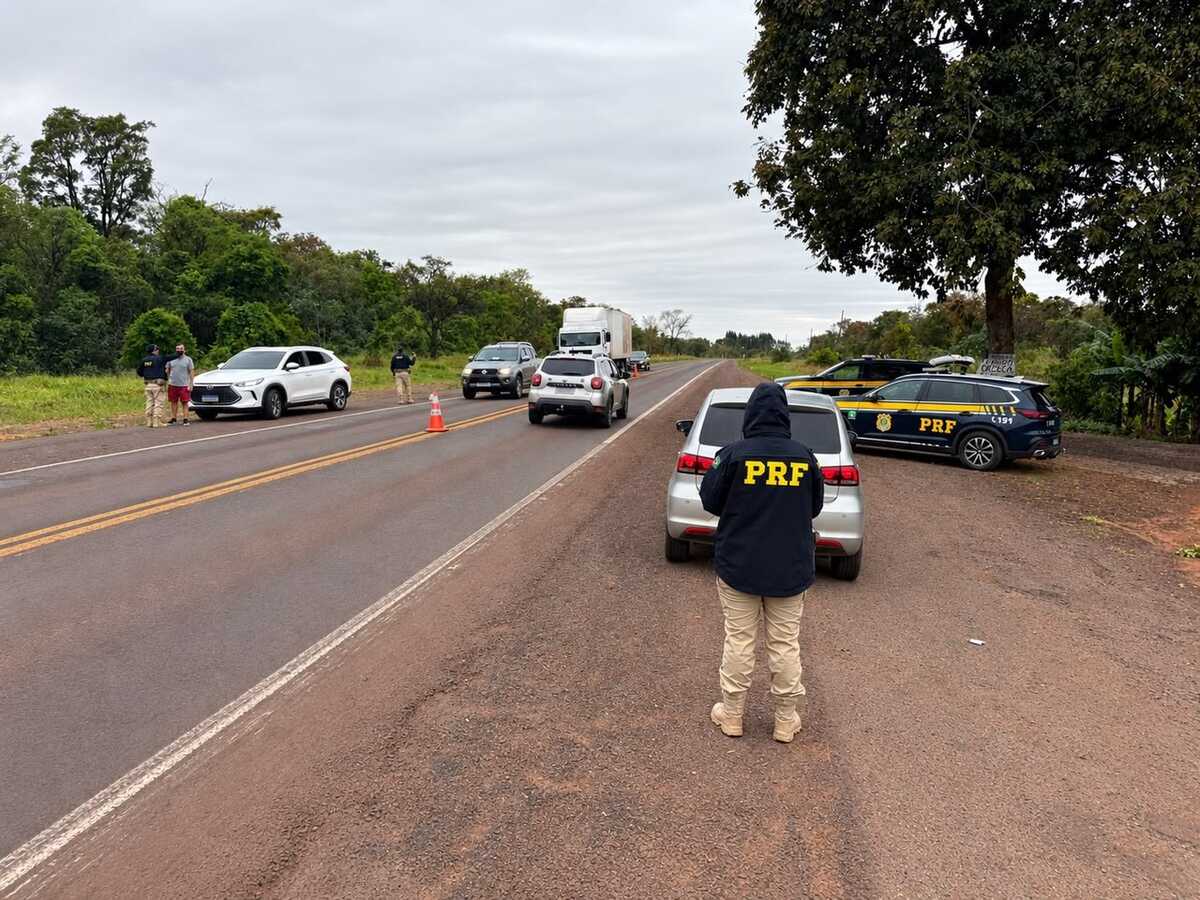 Policial rodoviário federal observa carros parados em fiscalização às margens de rodovia