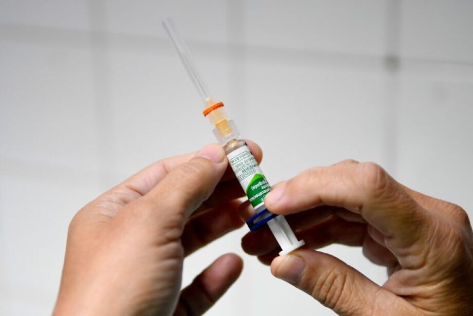 Mãos de profissional de saúde segurando seringa com dose de vacina