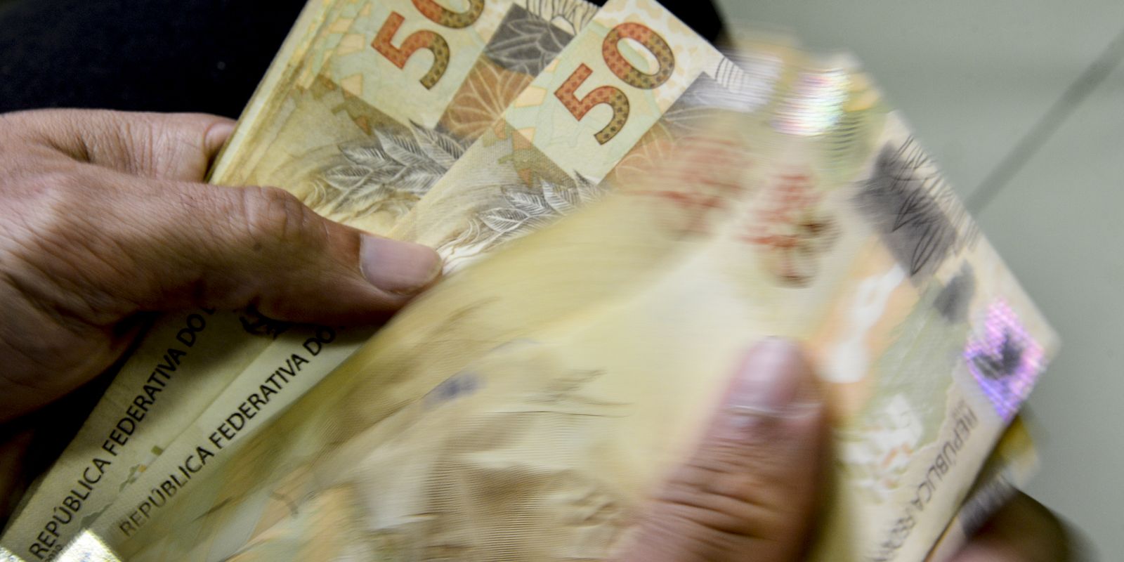 Mãos contando cédulas de 50 reais