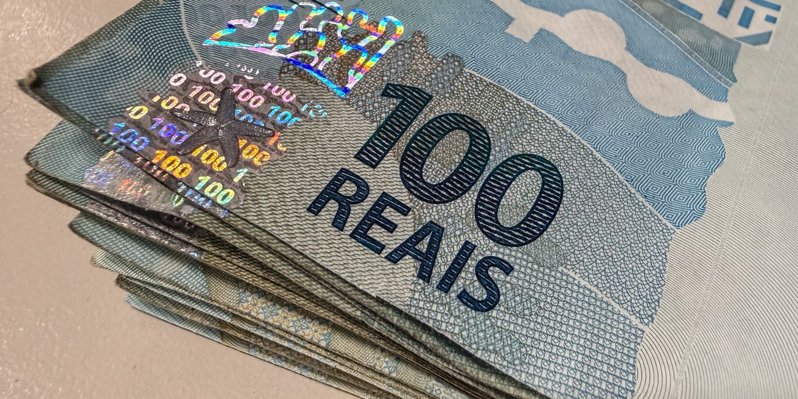 Maço de cédulas de 100 reais em close sobre uma superfície clara