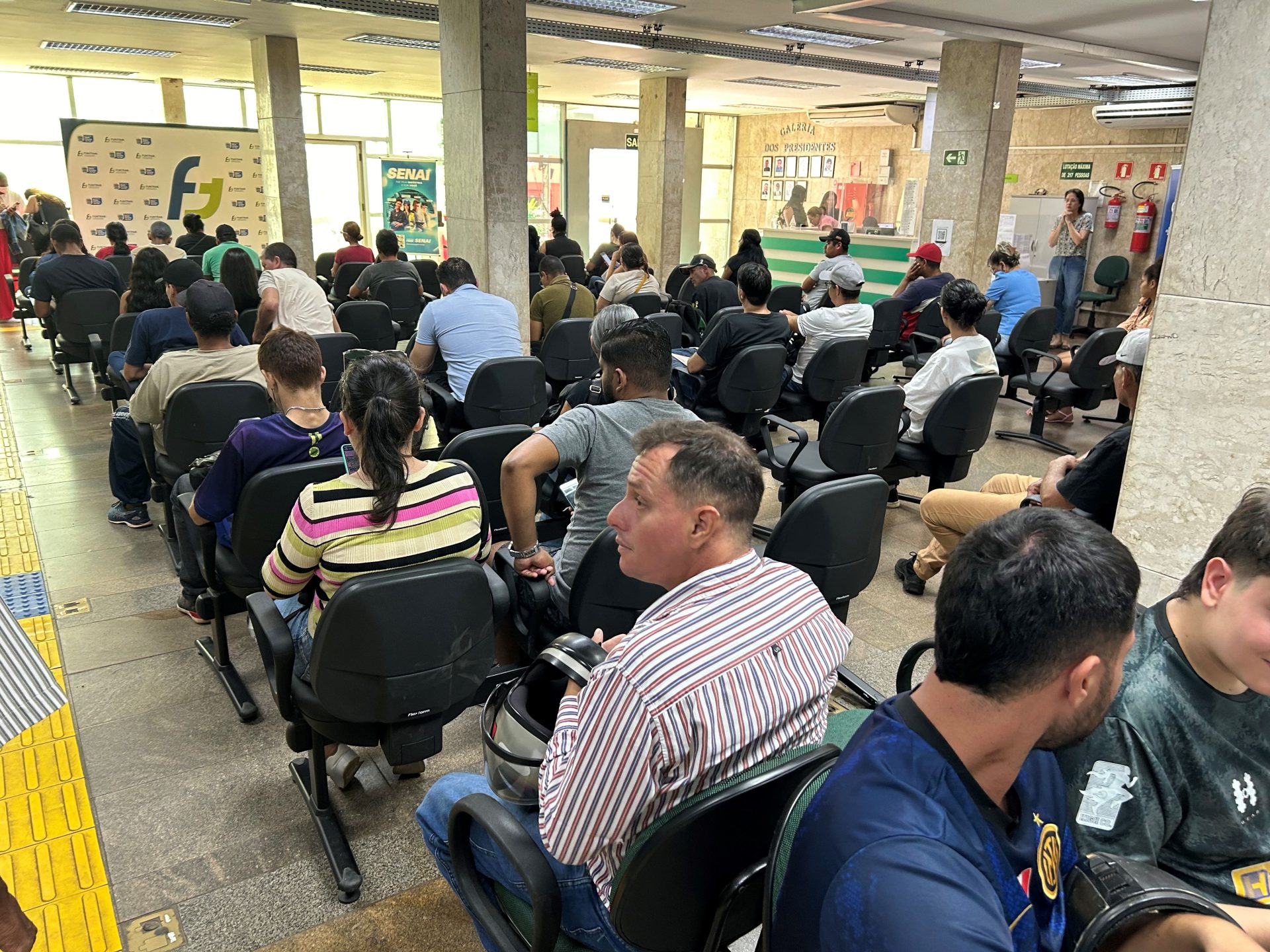 Sala de atendimento da Funtrab com várias pessoas sentadas em cadeiras aguardando
