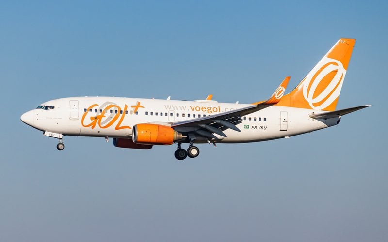 Boeing branco e laranja da Gol com trem de pouso baixado contra céu azul