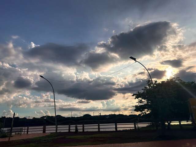 Nuvens escuras sobre o Lago do Amor, em Campo Grande, com postes e árvores em primeiro plano