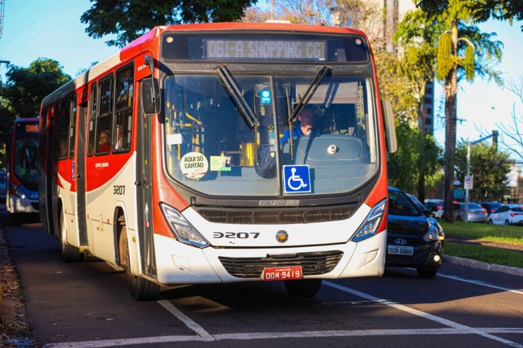 Ônibus urbano vermelho e branco do transporte coletivo de Campo Grande circulando em avenida arborizada