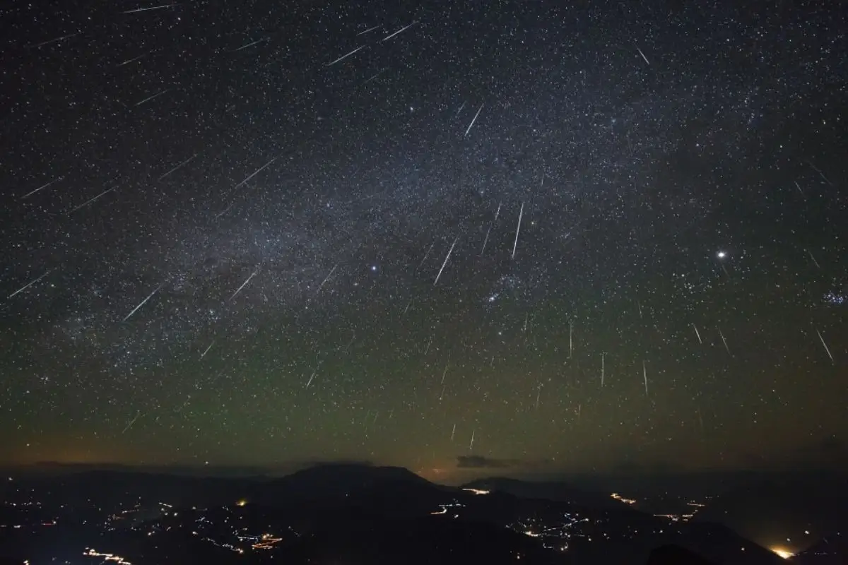 Vários rastros de meteoros em céu noturno sobre luzes de cidade no horizonte