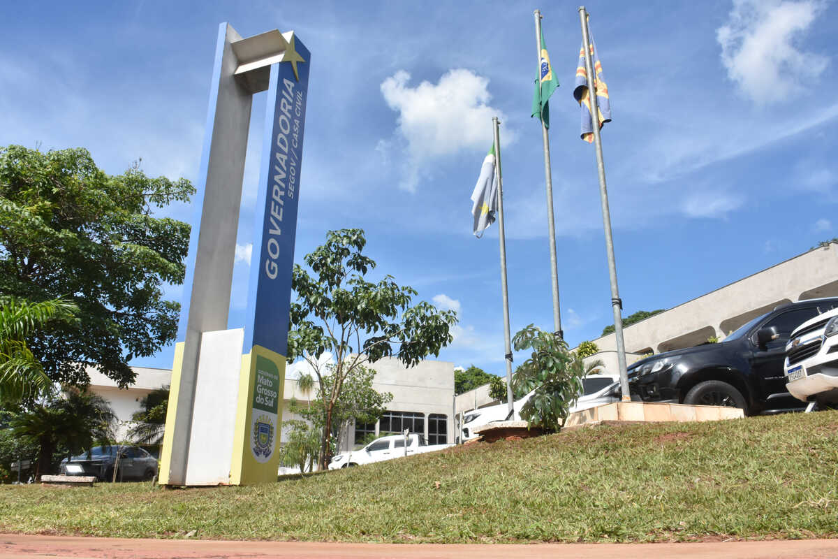 Totem com a palavra Governadoria e mastros com bandeiras em frente ao prédio do governo de Mato Grosso do Sul, no Parque dos Poderes, em Campo Grande