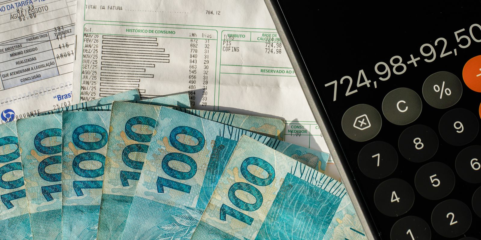 Cédulas de R$ 100 espalhadas sobre faturas com campos de tributos PIS e Cofins, ao lado de celular com calculadora aberta